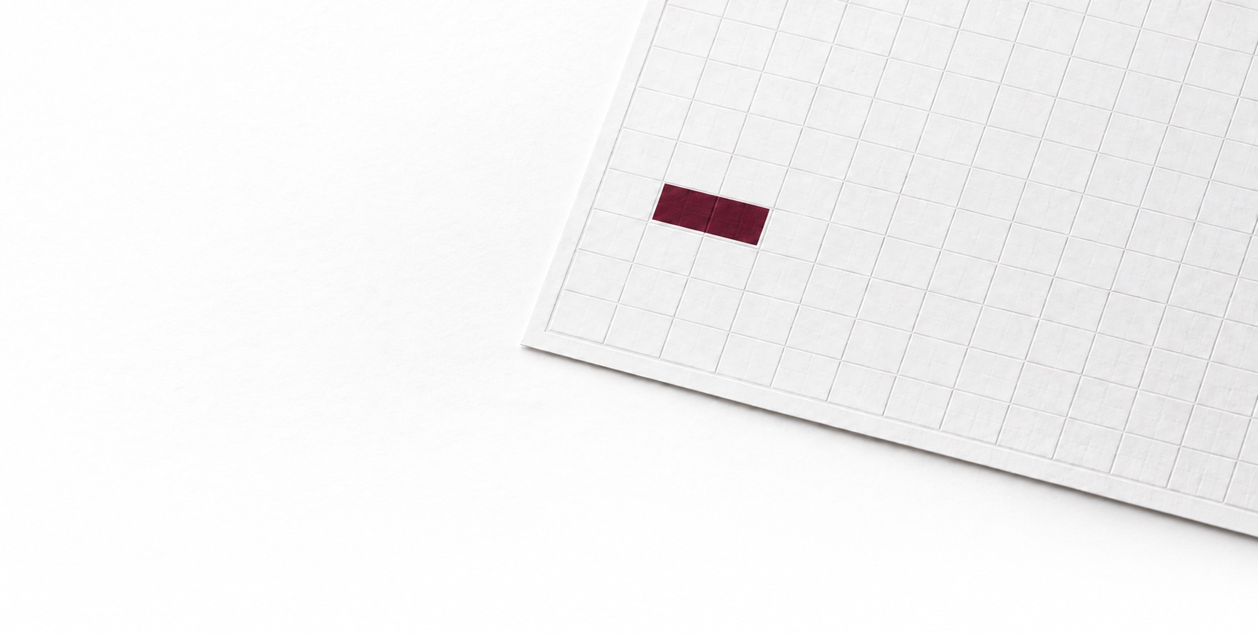 A fine white paper sheet with an embossed grid and a small burgundy rectangle.
